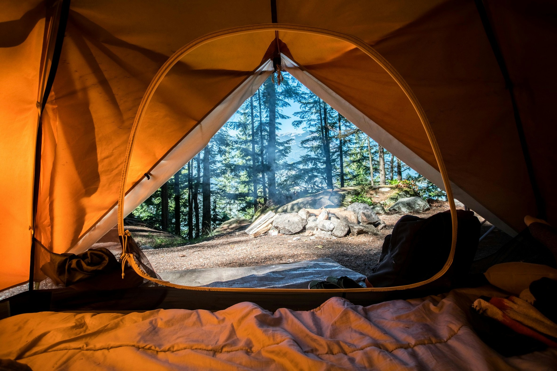 View out of a tent door onto a forest campsite and fire ring