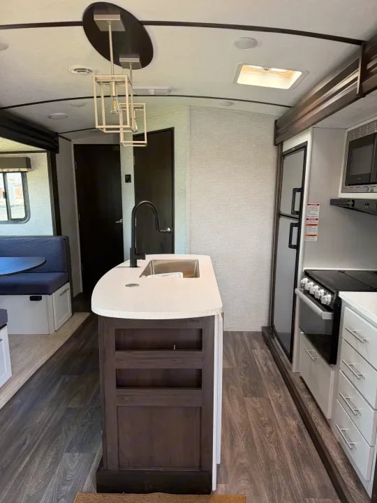 Kitchen island sink with pendant lighting, dinette, and refrigerator down the hall