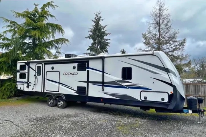 Exterior three-quarter view of the 38 ft travel trailer parked on gravel among tall trees