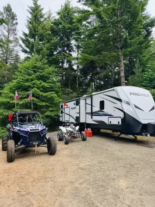 Trailer parked in the trees with two off-road vehicles beside it