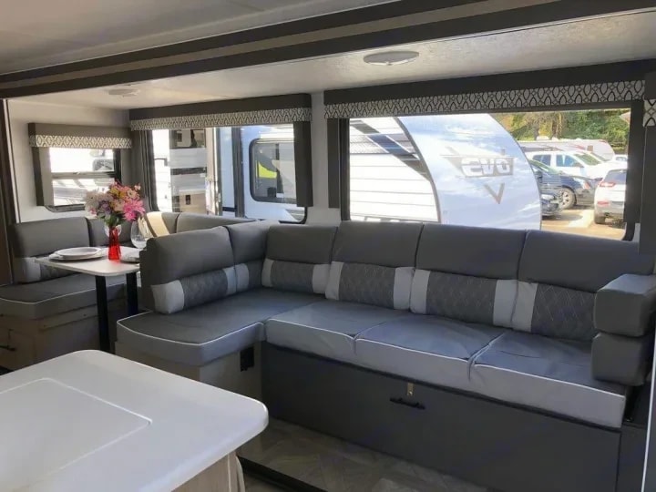 Dinette booth with flowers on the table and gray sectional sofa beyond