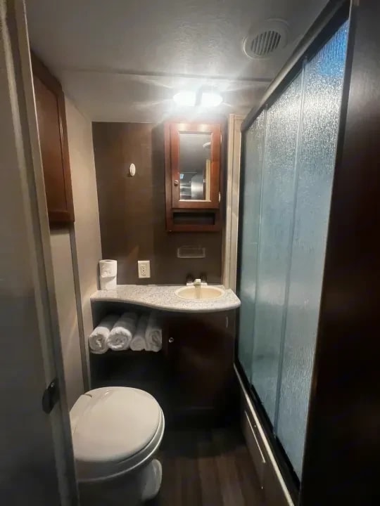 Bathroom with toilet, vanity sink, folded towels and sliding glass shower door