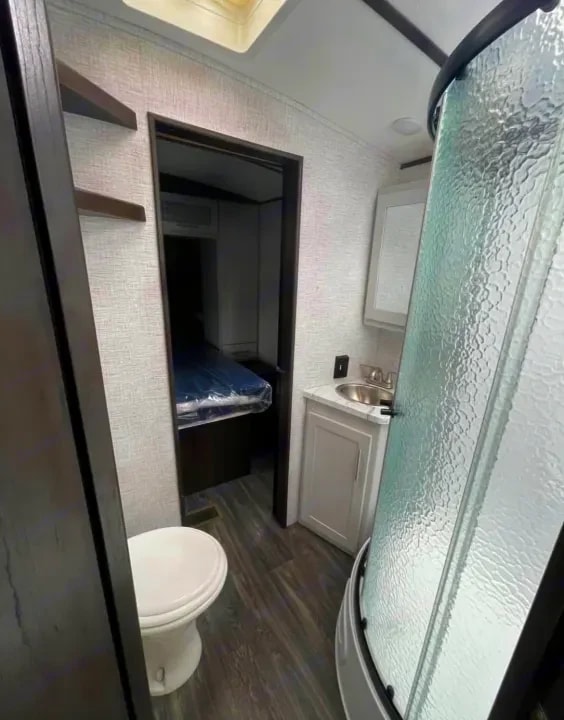Bathroom with corner shower, sink vanity, and toilet leading into a bedroom