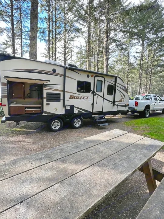 Trailer hitched to a white pickup truck at a campsite with a picnic table in the foreground