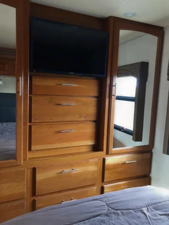 Bedroom dresser with mounted TV, drawers, and mirrored wardrobe doors