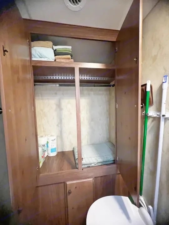 Open closet with hanging rod, shelf, and folded linens