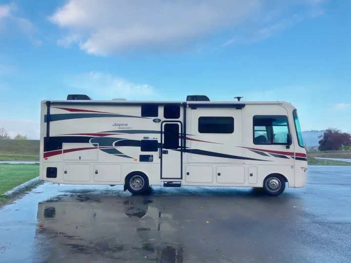 Passenger-side exterior profile of the Class A motorhome parked on wet pavement