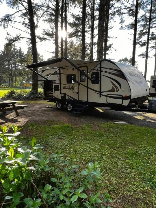 Trailer with awning extended at a wooded campsite in late-day sun