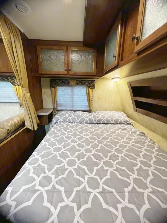 Queen bed with quilted gray coverlet and wood cabinetry overhead