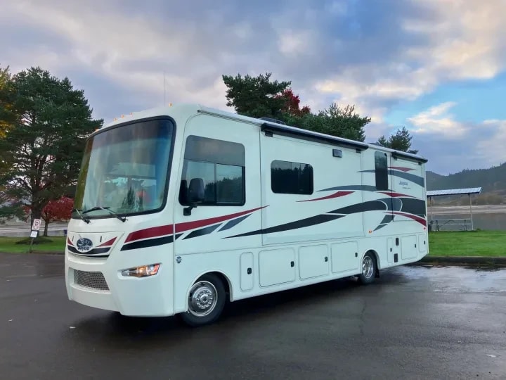 Front three-quarter exterior view of the motorhome parked near a lake at dusk