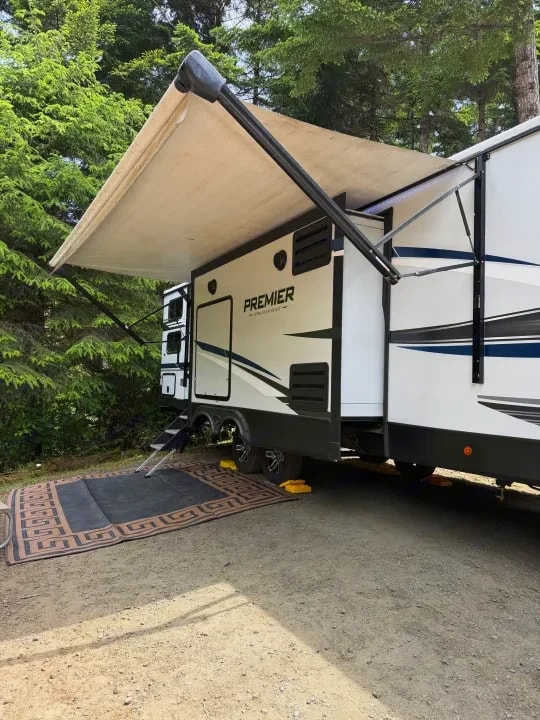 Awning and side of trailer with steps down and rug laid out at campsite