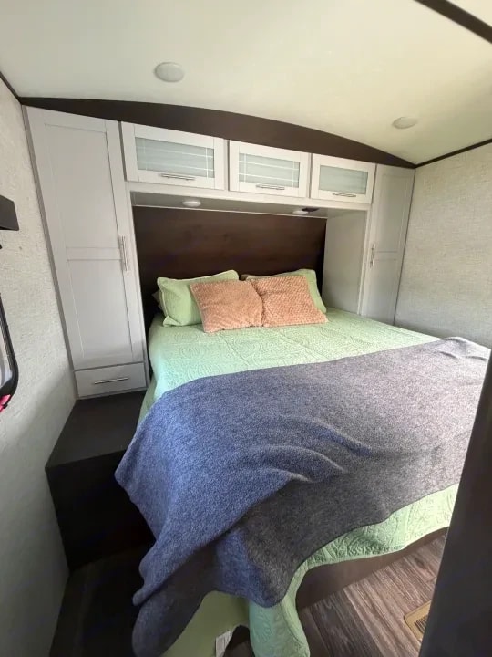 Bedroom with queen bed, green bedding, throw blanket, and overhead cabinets