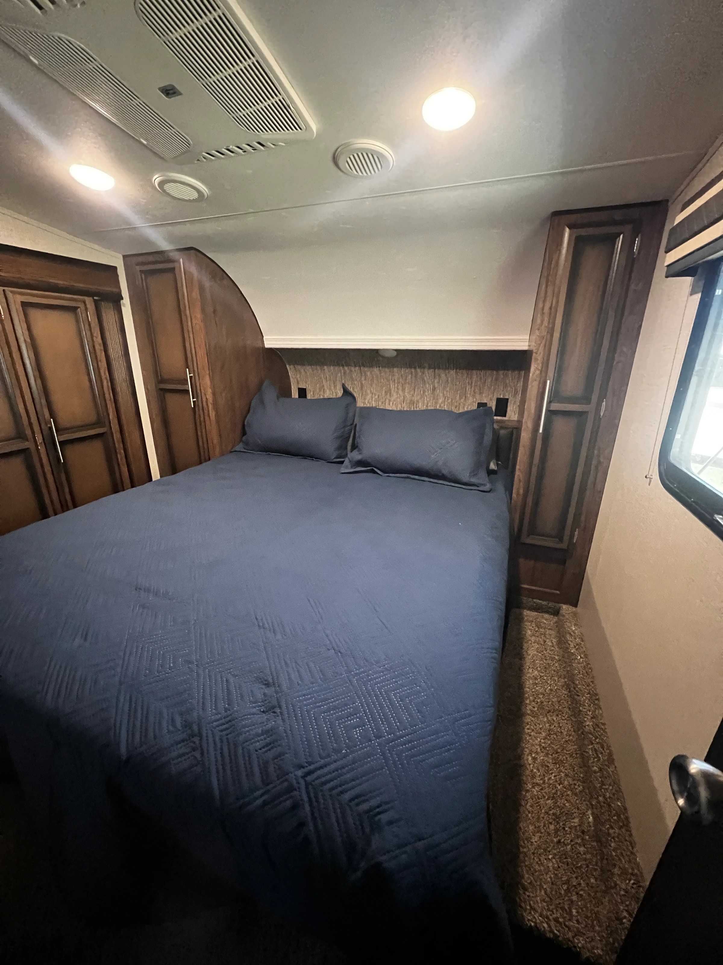 Primary bedroom with made bed, dark quilt, and wood wardrobe cabinets