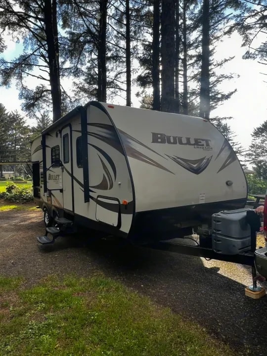 Three-quarter view of the Bullet travel trailer parked among tall pine trees