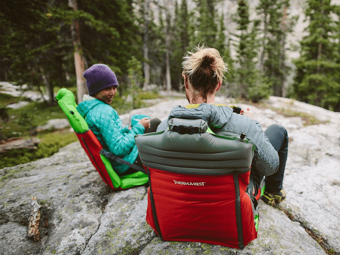 Two campers sitting in pad-and-sleeve camp chairs on a granite slab