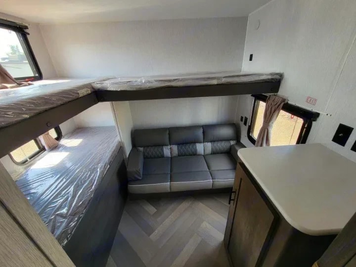 Bunk room with jiffy sofa below and upper bunk bed still wrapped in plastic