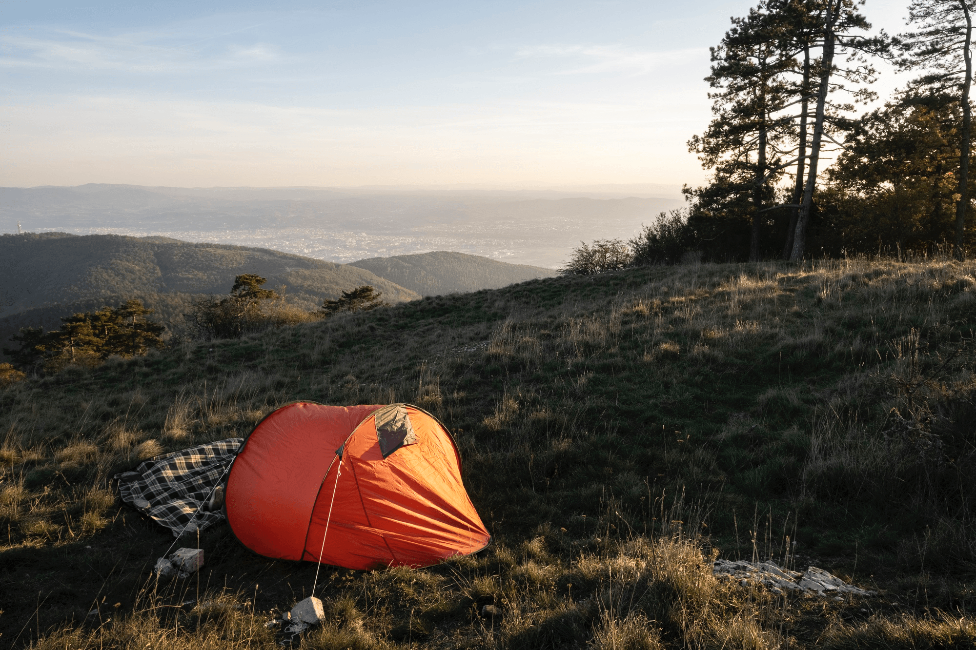 Orange pop-up tent pitched on a grassy ridge at sunrise